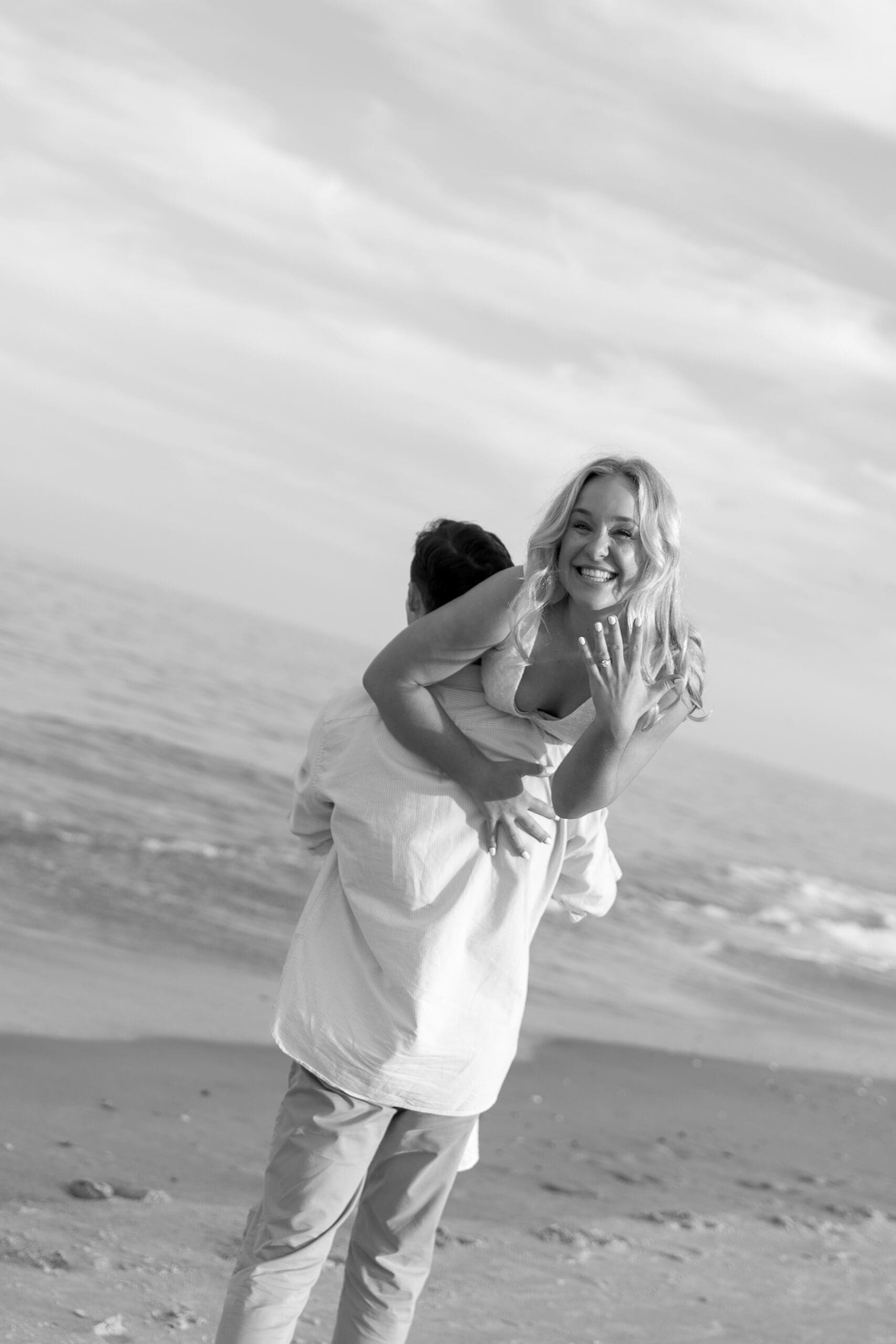 Groom scooping up bride as she flashes her ring at camera