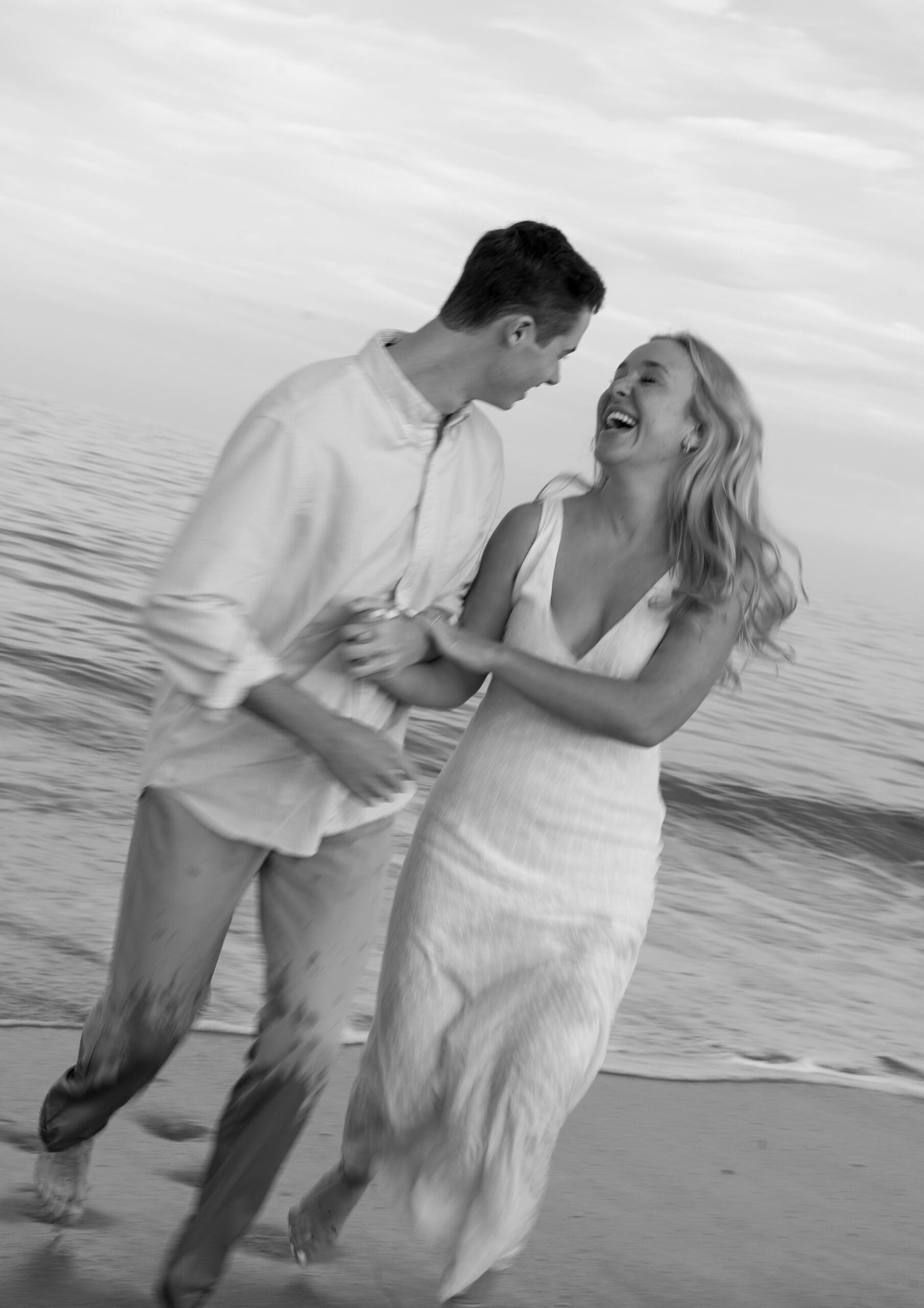 Couple running away from the ocean laughing into each others arms