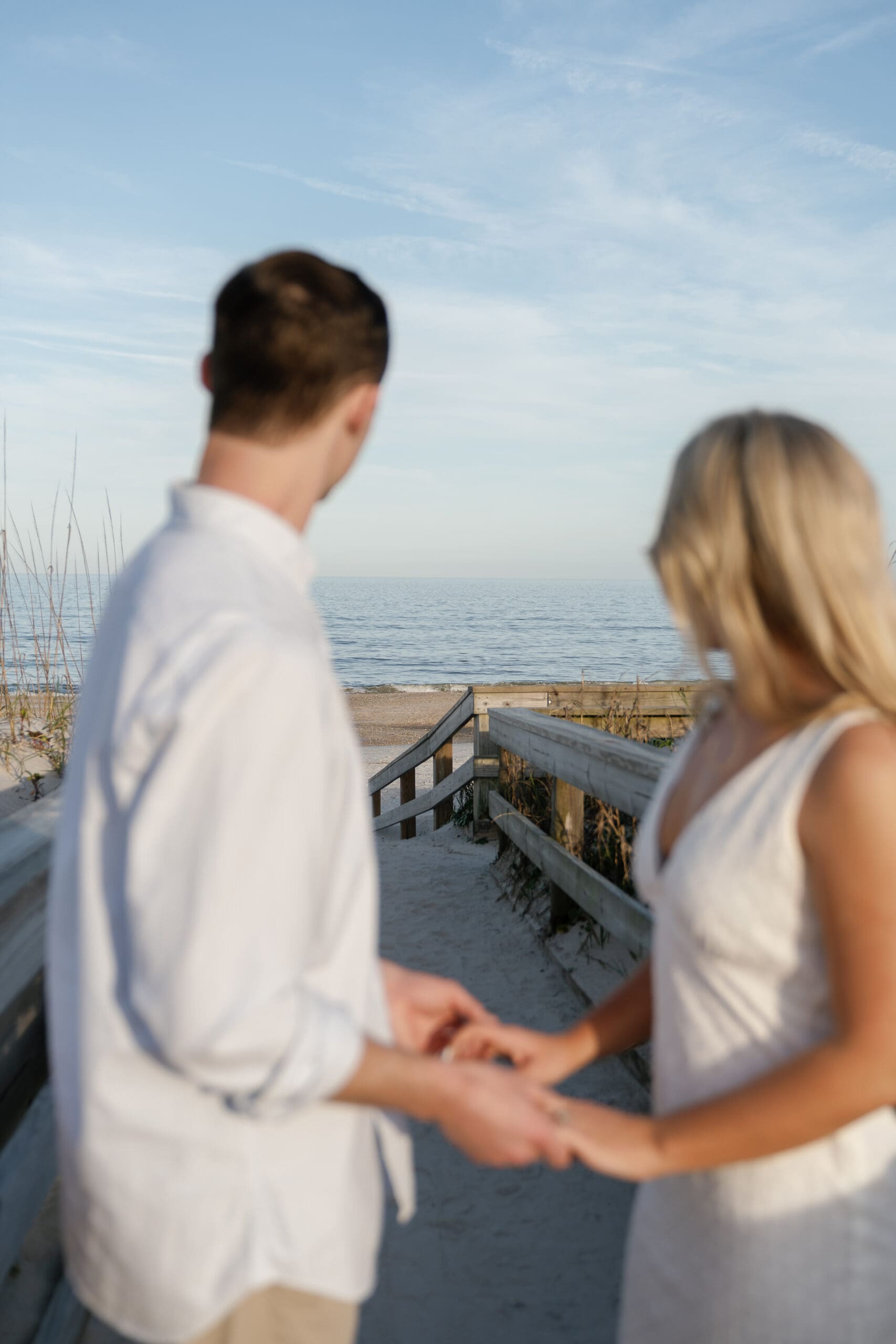 Couple holding hands on boardwalk looking out at the ocean for beach engagement session