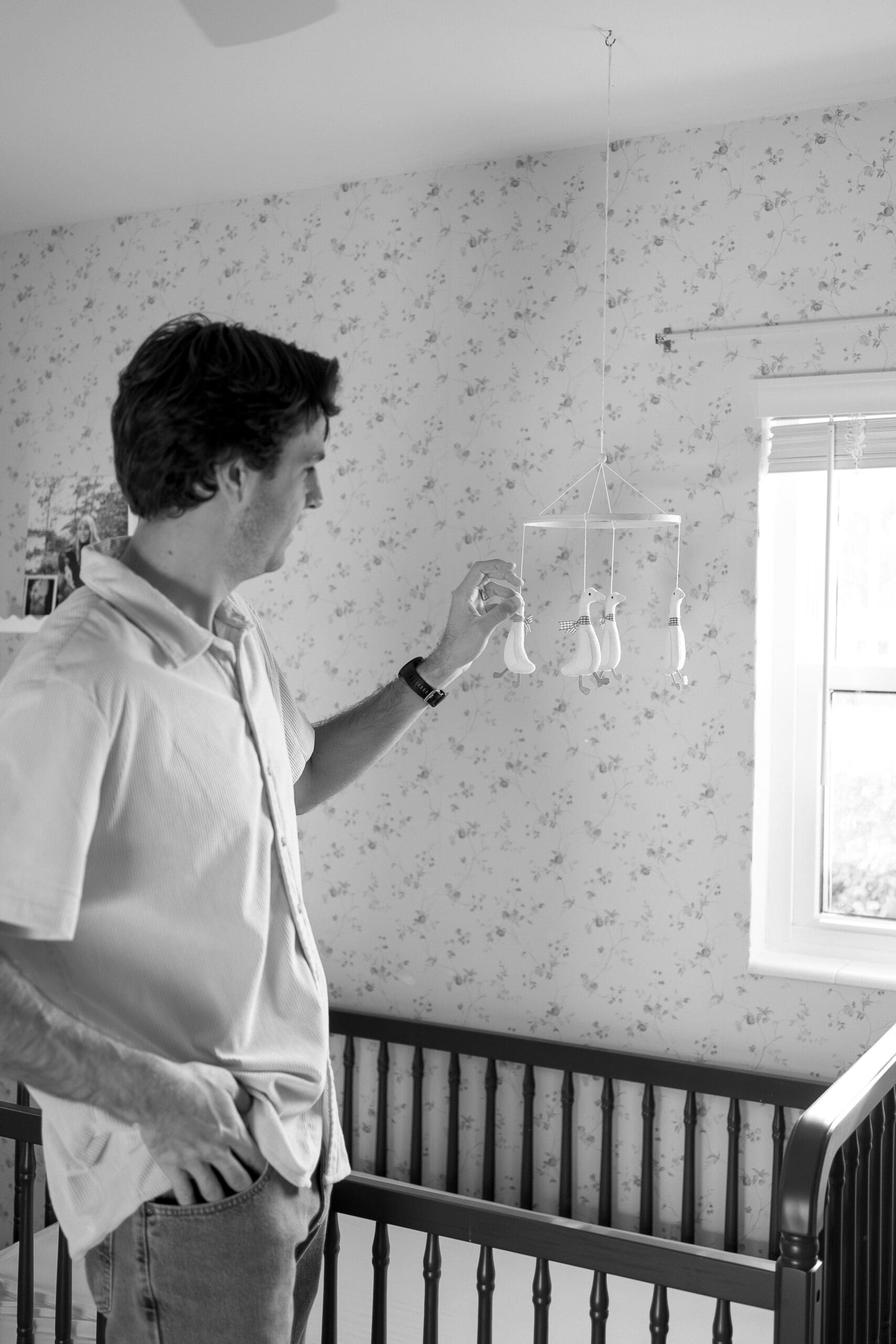 Dad playing with a baby mobile above crib in nursery