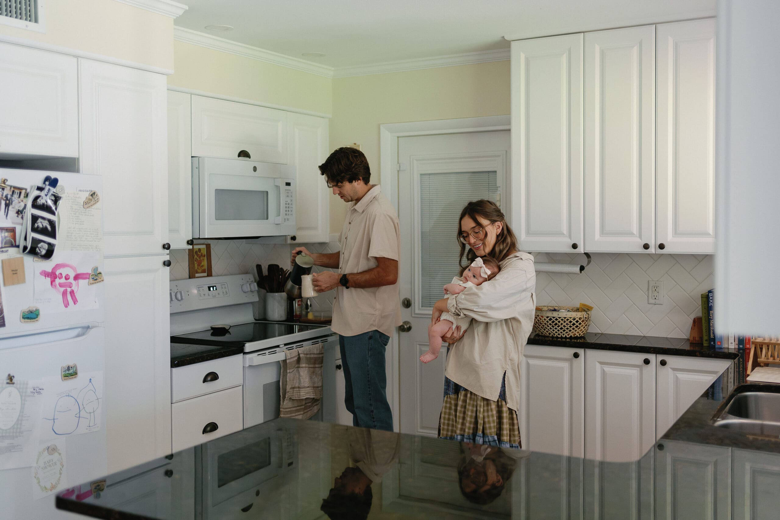 Dad making coffee in kitchen and mom holding newborn baby