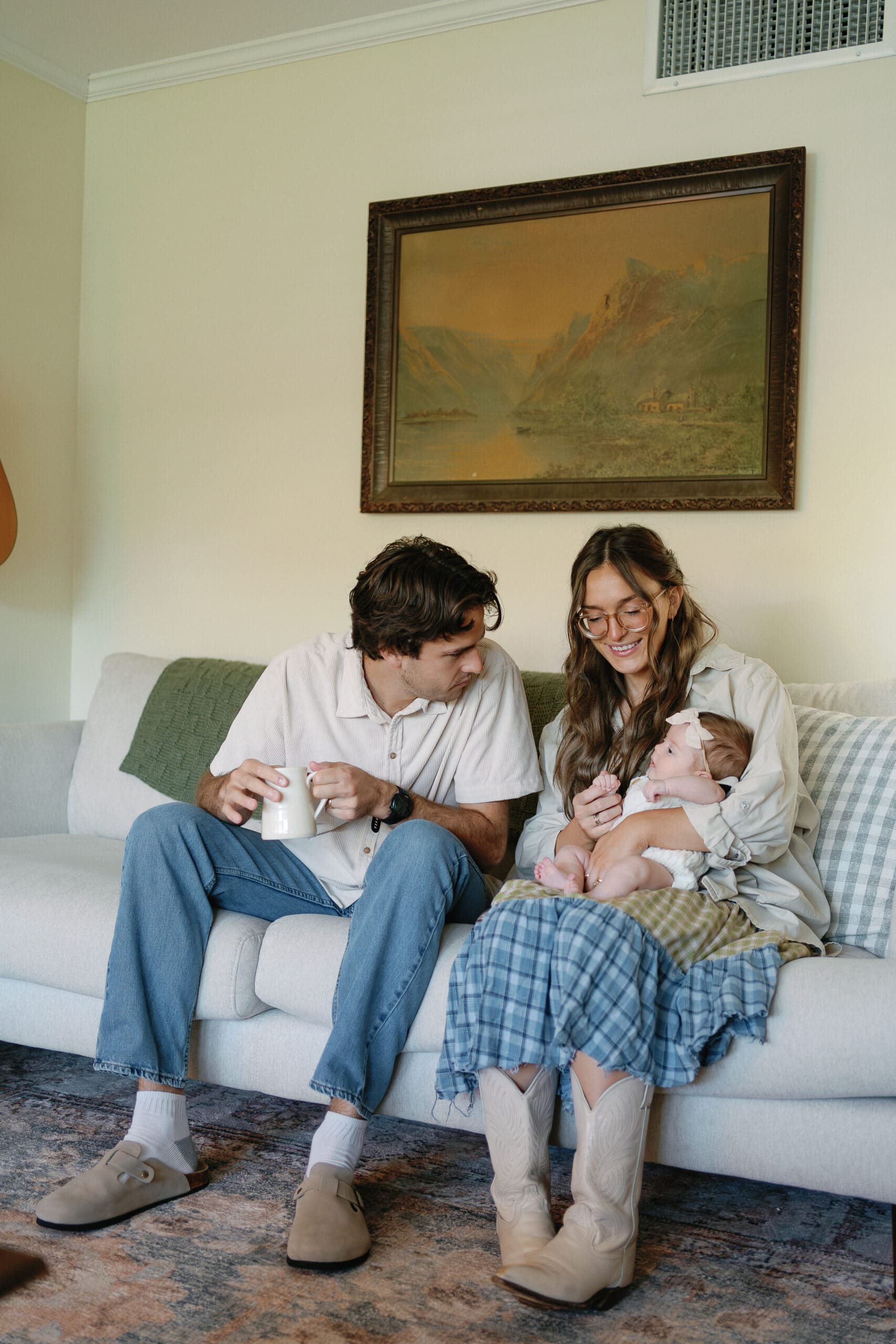 Parents sitting on couch at home drinking coffee and looking at their baby
