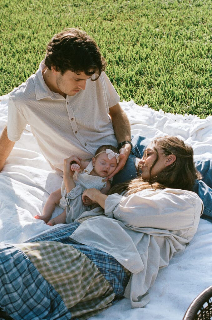 Couple laying down on blanket with baby outside