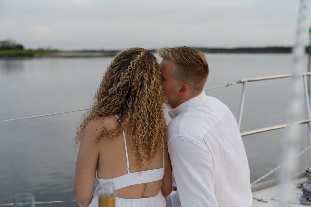 Couple whispering in each others ear while sitting on a sailboat