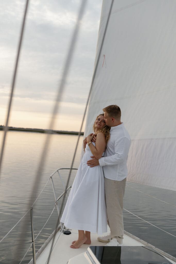 Couple wrapped up in each others arms and looking at each other while sailing on a boat by Shelby Ann Photos