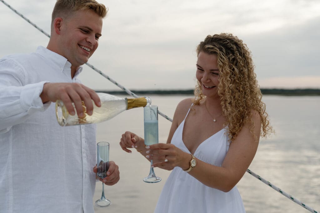 Couple pouring champagne and laughing while on a sailboat by Shelby Ann Photos