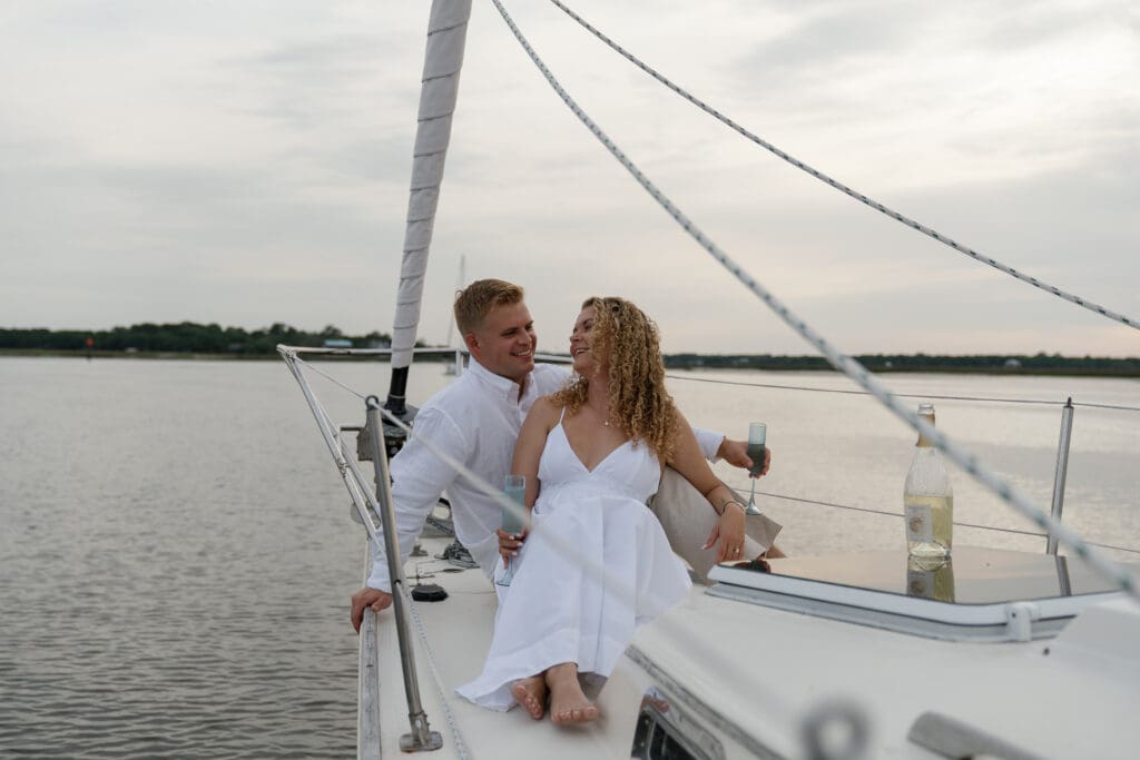 Couple sitting on the bow of a sailboat drinking champagne by Shelby Ann Photos