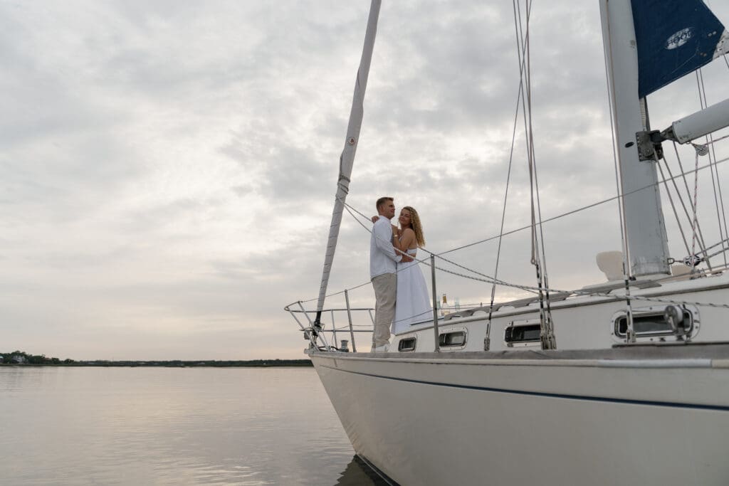 Wide shot of couple standing on the front of a sailboat, posing for engagement session by Shelby Ann Photos